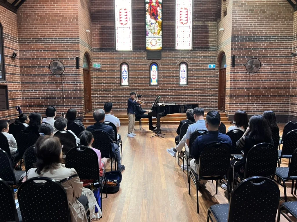 Two student violinists performing a duet with piano at a recital