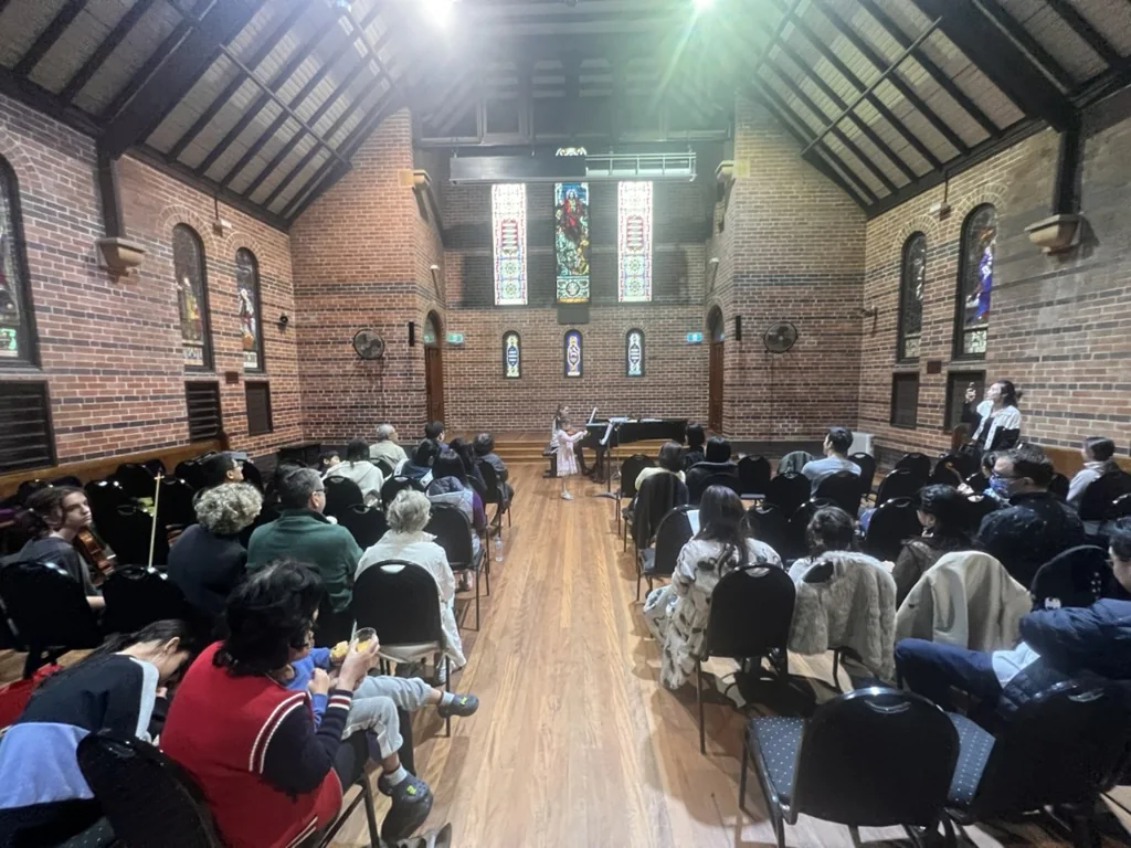 Young violinist performing with piano for an audience in a heritage concert hall
