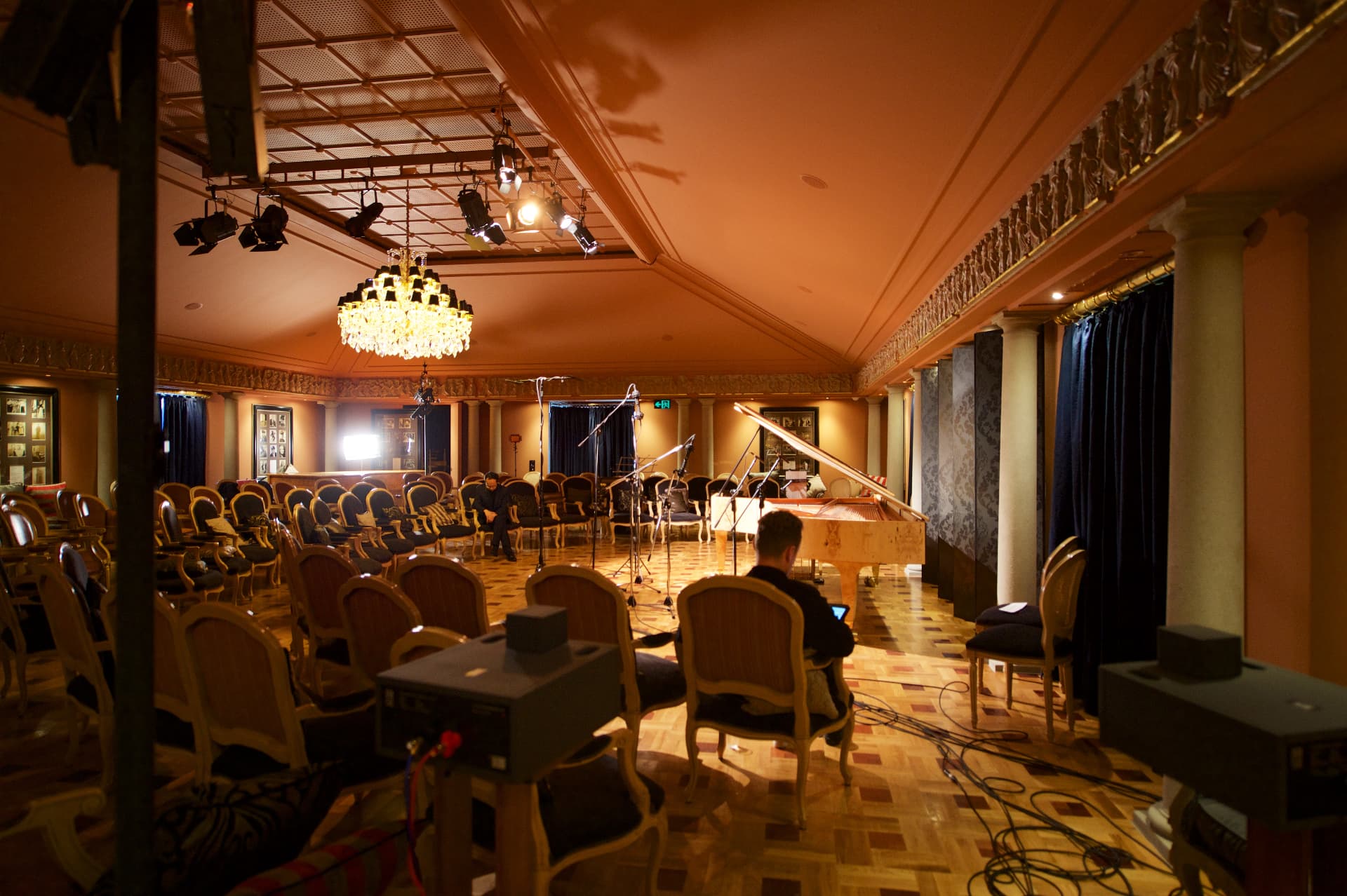 Concert salon with chandelier, rows of gilt chairs and a grand piano during a recording