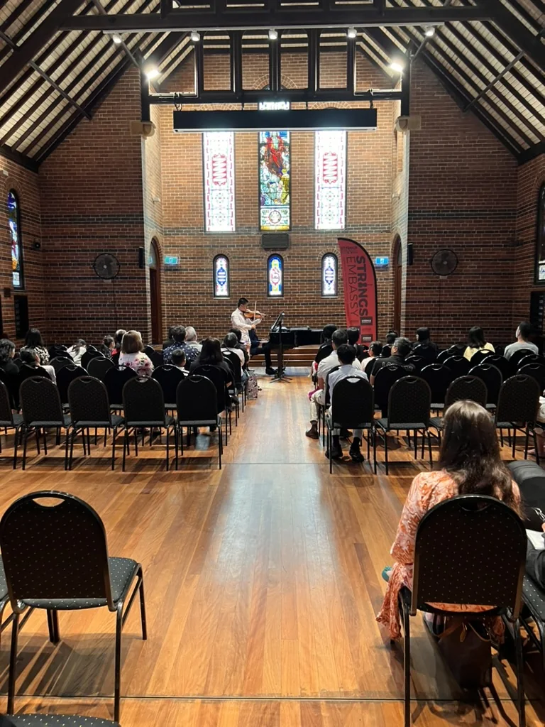 Student violinist performing on stage before a recital audience