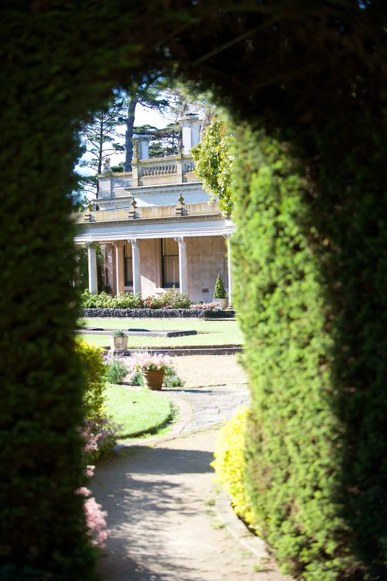 View of the mansion framed by a clipped hedge archway and garden path